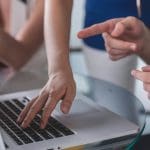 Two people using a laptop with one pointing at the screen